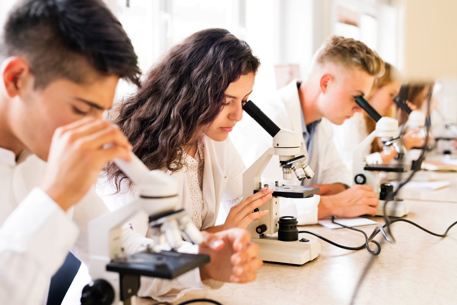 Beautiful high school students with microscopes in laboratory during biology class.