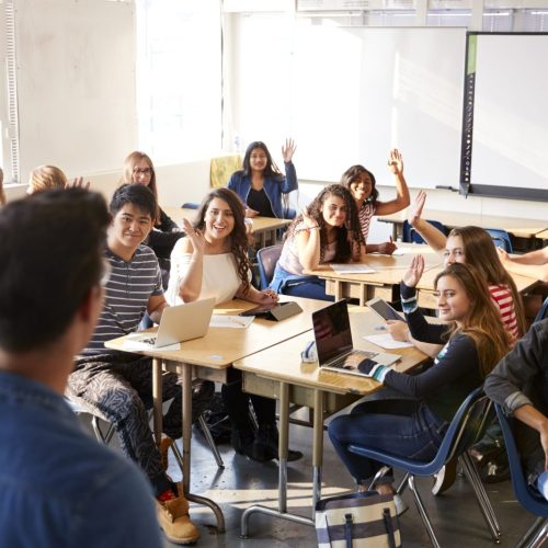 Rear View Of Male High School Teacher Standing At Front Of Class Teaching Lesson